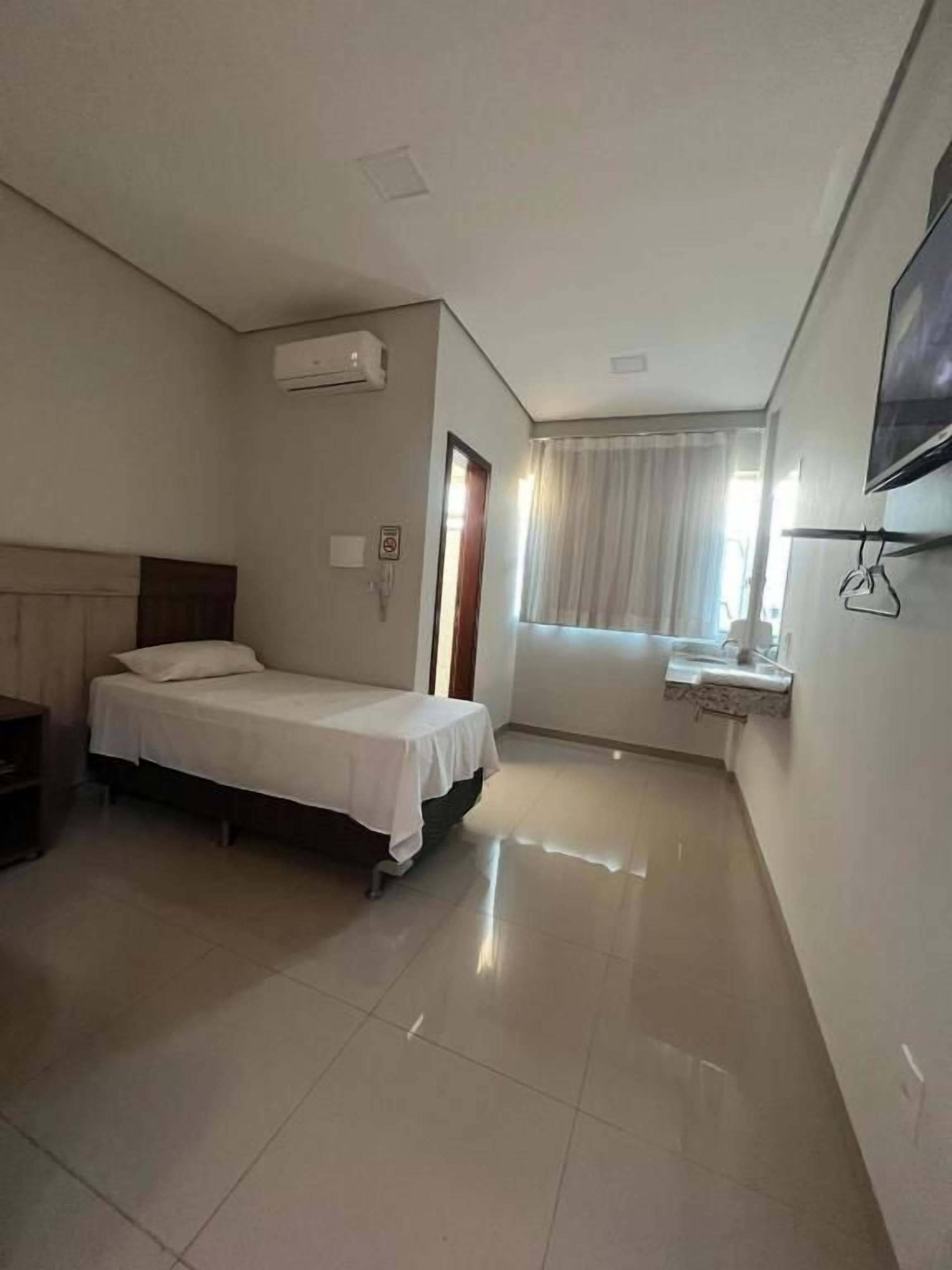 Una habitación de hotel con una cama, un escritorio pequeño, una ventana con cortinas y un televisor montado.