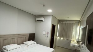 Quarto de hotel com uma cama grande, televisão, banheiro com espelho e ar condicionado.