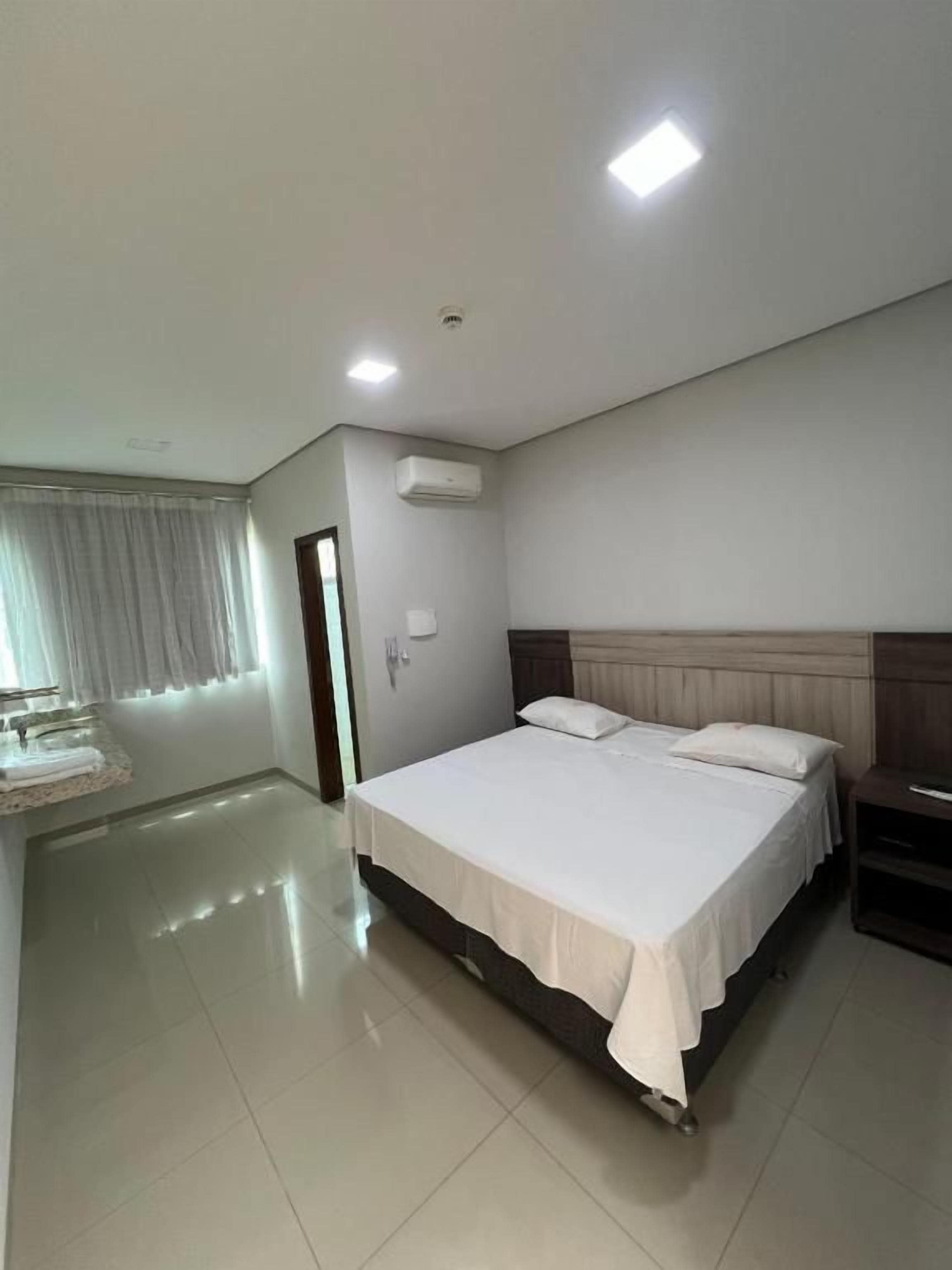 A hotel room with a large bed, a bedside table, a wardrobe, and a window with curtains.