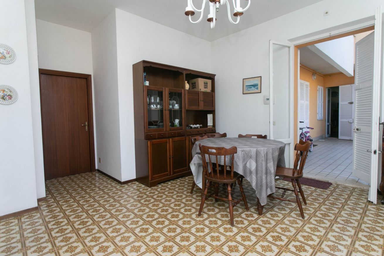 Uma sala de jantar com uma mesa redonda, cadeiras, um armário com portas de vidro e ladrilhos no chão com padrão.