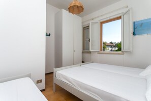 A bedroom with a single bed, a window with an open shutter, and a view of the outside.
