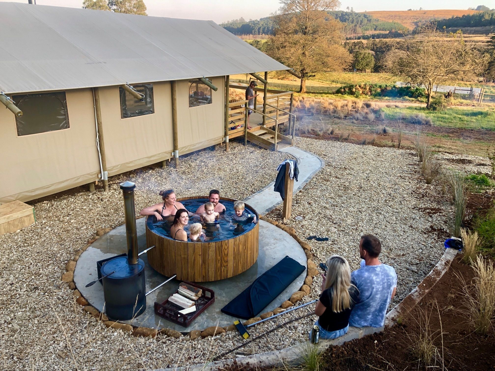 A hot tub with five people, surrounded by a wooden deck and a covered area.