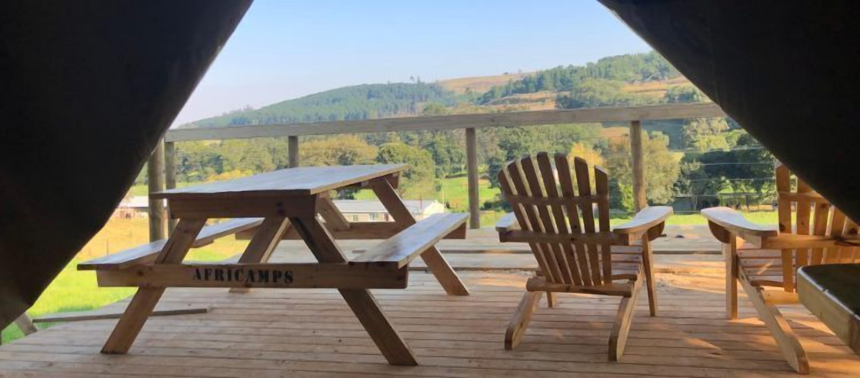 Una terraza de madera con mesas de picnic y sillas Adirondack con vistas a un paisaje montañoso.