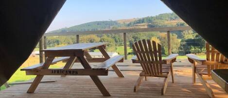 Una terraza de madera con mesas de picnic y sillas Adirondack con vistas a un paisaje montañoso.