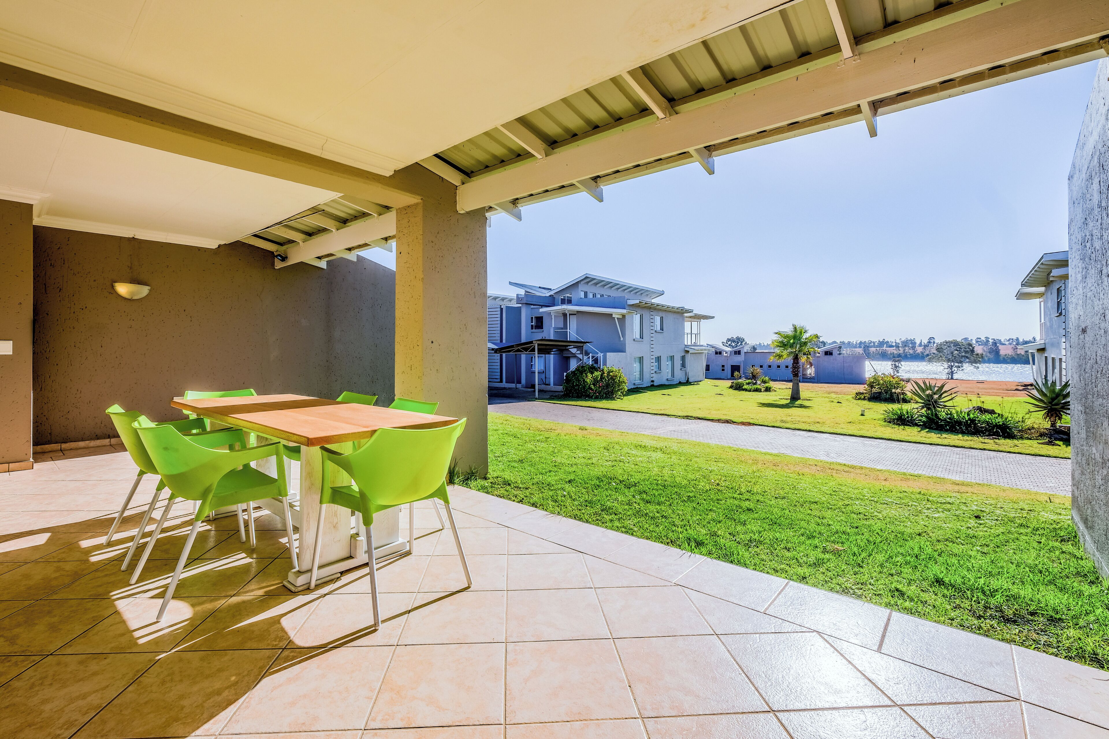 A covered patio area with a table and chairs, a view of a residential area with houses and a lawn.