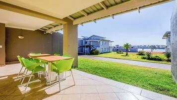 A covered patio area with a table and chairs, a view of a residential area with houses and a lawn.