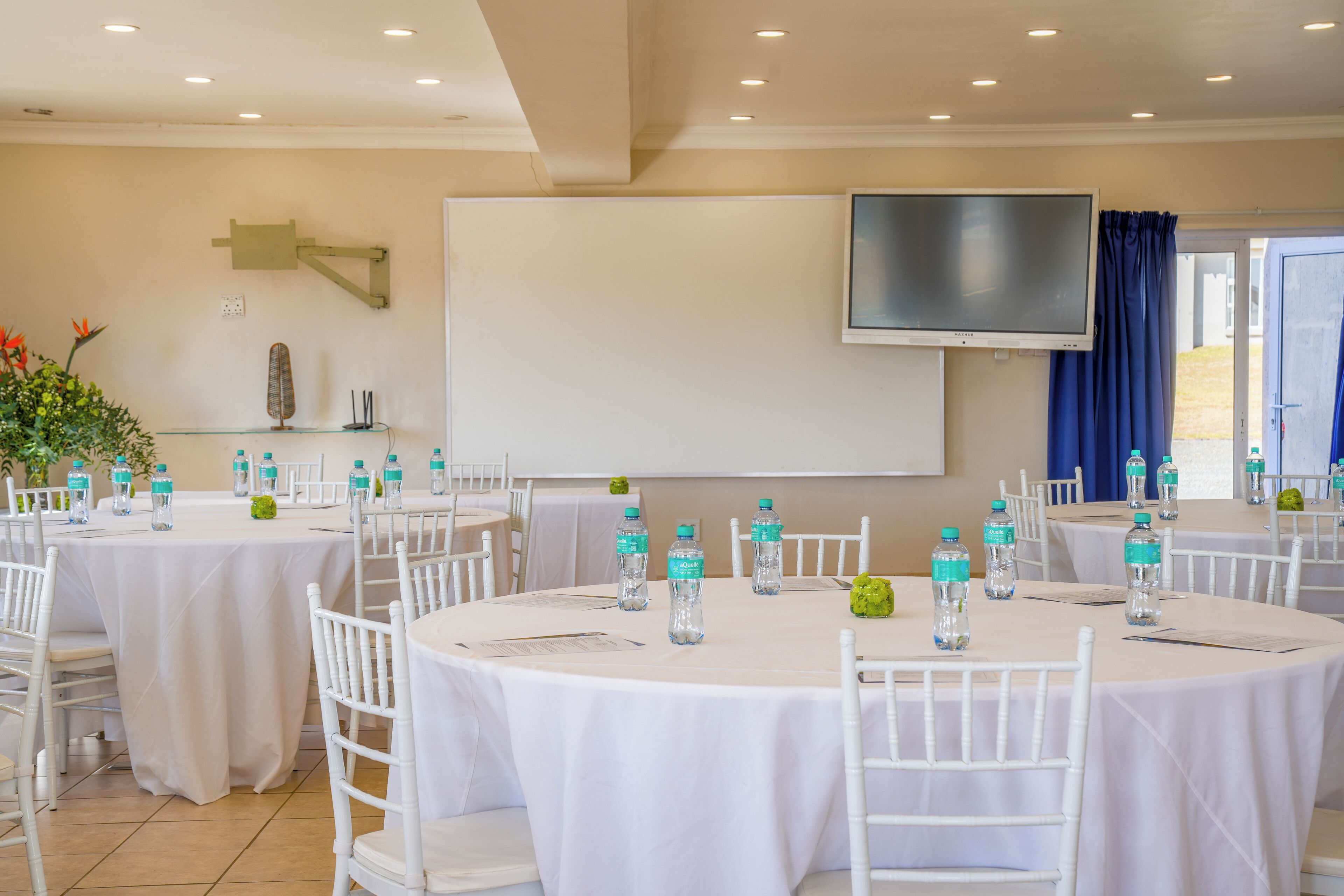 Un salón de conferencias con mesas y sillas blancas, y una pantalla grande.