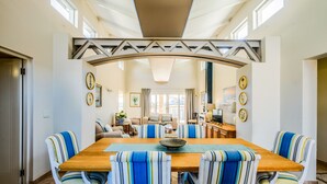 A spacious dining area with a wooden table, striped upholstered chairs, and a view into a living room with a sofa and TV. - The Anchorage (Vaal Marina)
