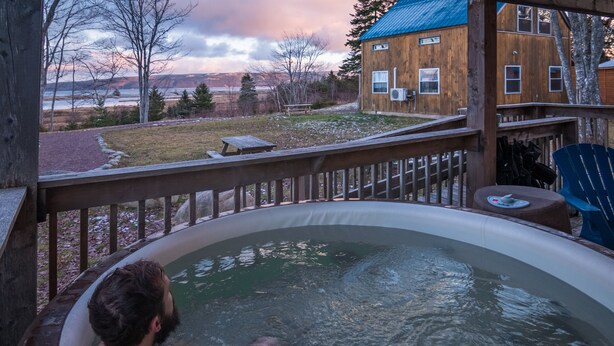 A hot tub with a wooden deck and a view of a house and landscape.
