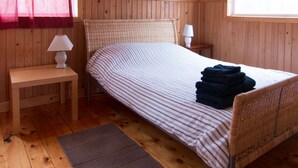 A wooden-paneled bedroom with a bed, bedside lamps, a ceiling fan, a window with a view, and a framed picture on the wall.