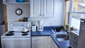 A kitchen with white cabinets, a stove, a coffee maker, and a window with a view of a wooden building.