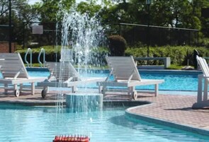 Una piscina con fuente de agua, sillas de descanso y un camino de ladrillos.