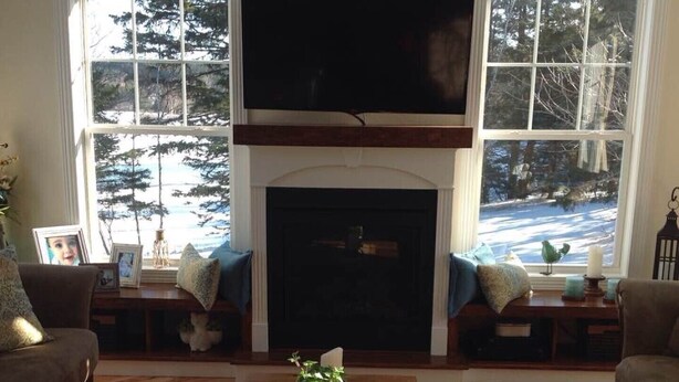 A living room with a fireplace, two sofas, a coffee table, and large windows with a view of trees and snow. - Beautiful water's edge 2 bedroom vacation home (Breadalbane)