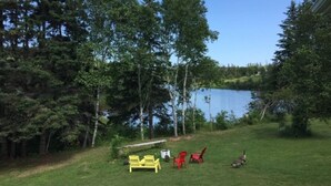 A grassy area with a lake, trees, and outdoor furniture. - Beautiful water's edge 2 bedroom vacation home (Breadalbane)