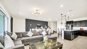 Una sala de estar moderna con un sofá gris, una mesa de centro de vidrio y una cocina con armarios oscuros y una isla central.