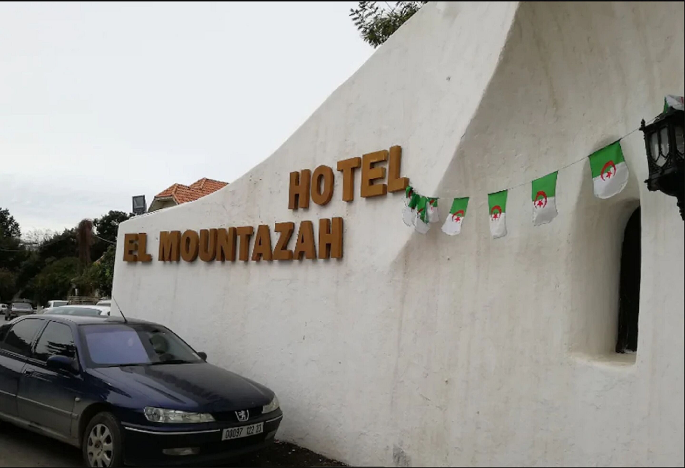 Señal de hotel con el nombre "HOTEL EL MOUNTAZAN" y un coche estacionado en la calle.
