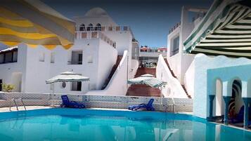 Un espace piscine avec des chaises longues bleues et un escalier menant à un bâtiment blanc surmonté d’un dôme.