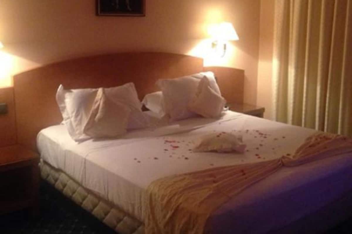 Une chambre d’hôtel avec un lit, des oreillers, une table de chevet, une lampe et un tableau au mur.