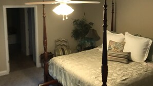 Un lit à baldaquin, une table de chevet, une lampe et une chaise avec un coussin à motifs.