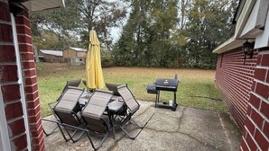Une terrasse extérieure avec une table et des chaises, un barbecue et un parasol jaune.