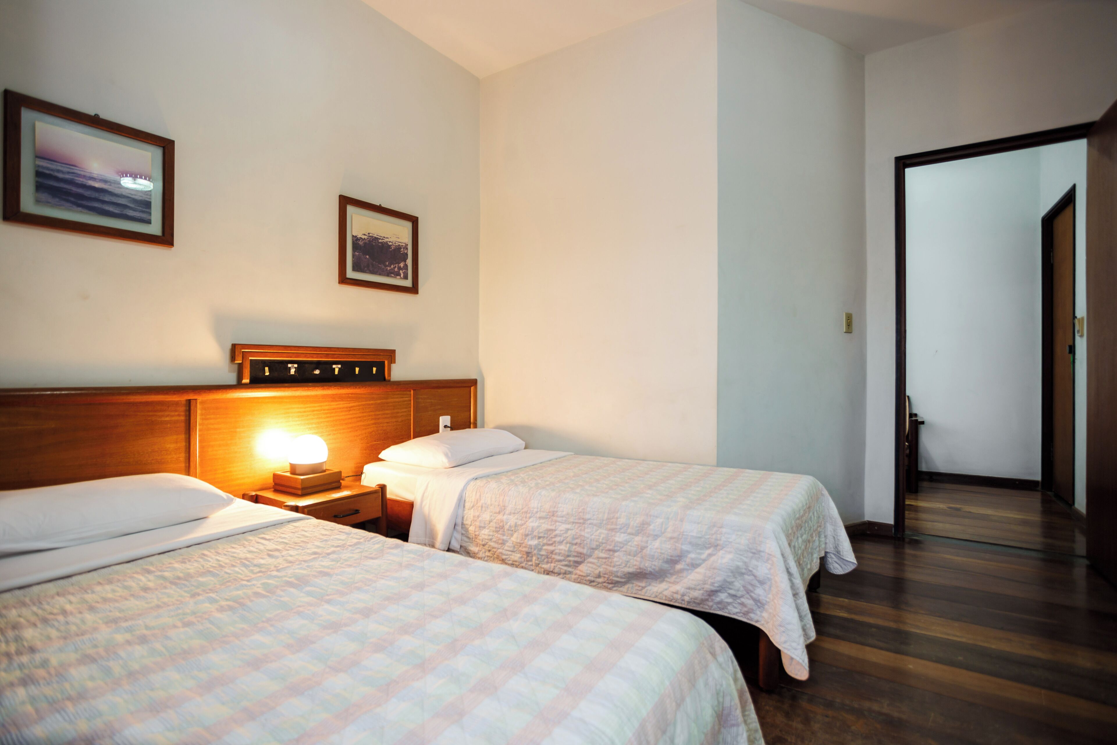 A hotel room with two beds, a nightstand with a lamp, and a wooden headboard.