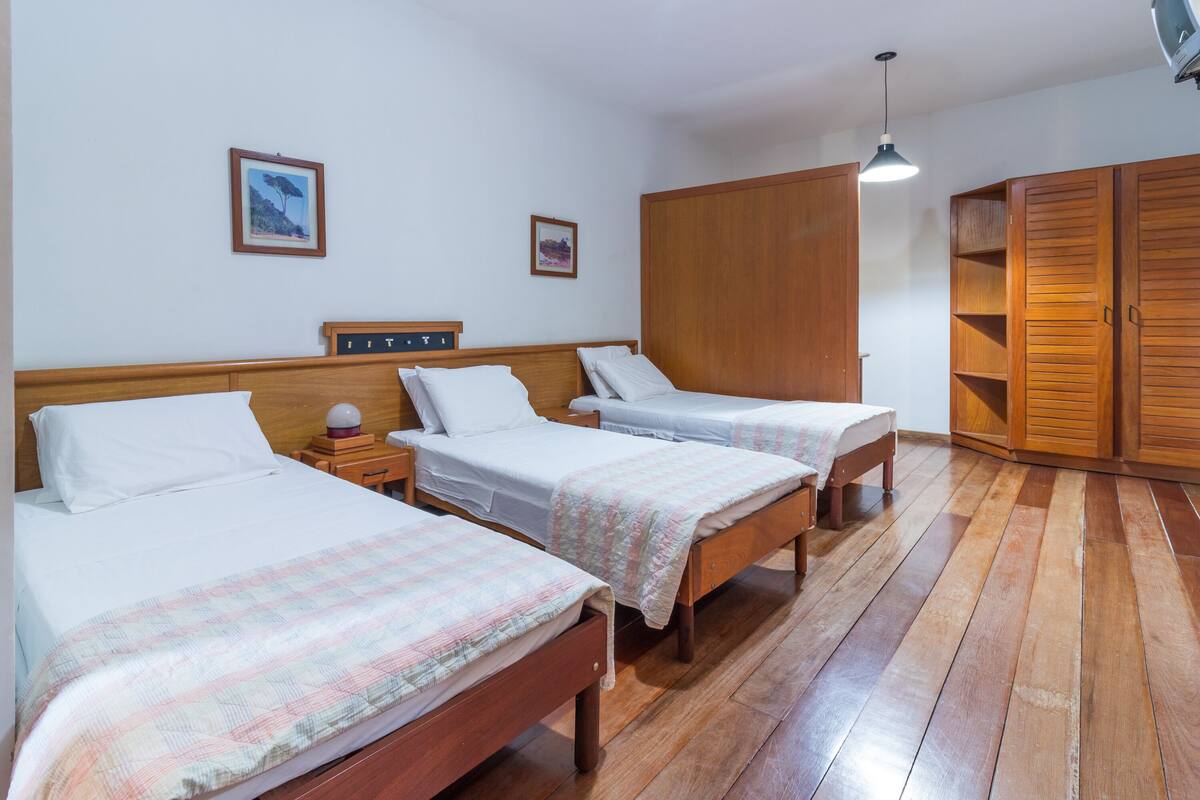 Habitación de hotel con tres camas de madera, un armario y una mesita de noche pequeña con lámpara.