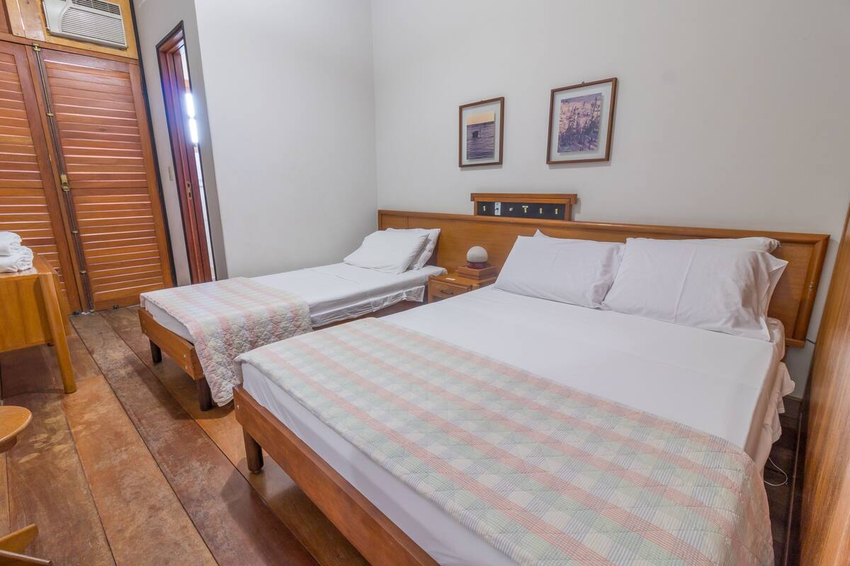 Habitación de hotel con dos camas individuales, un armario de madera, una mesita y aire acondicionado instalado en la pared.