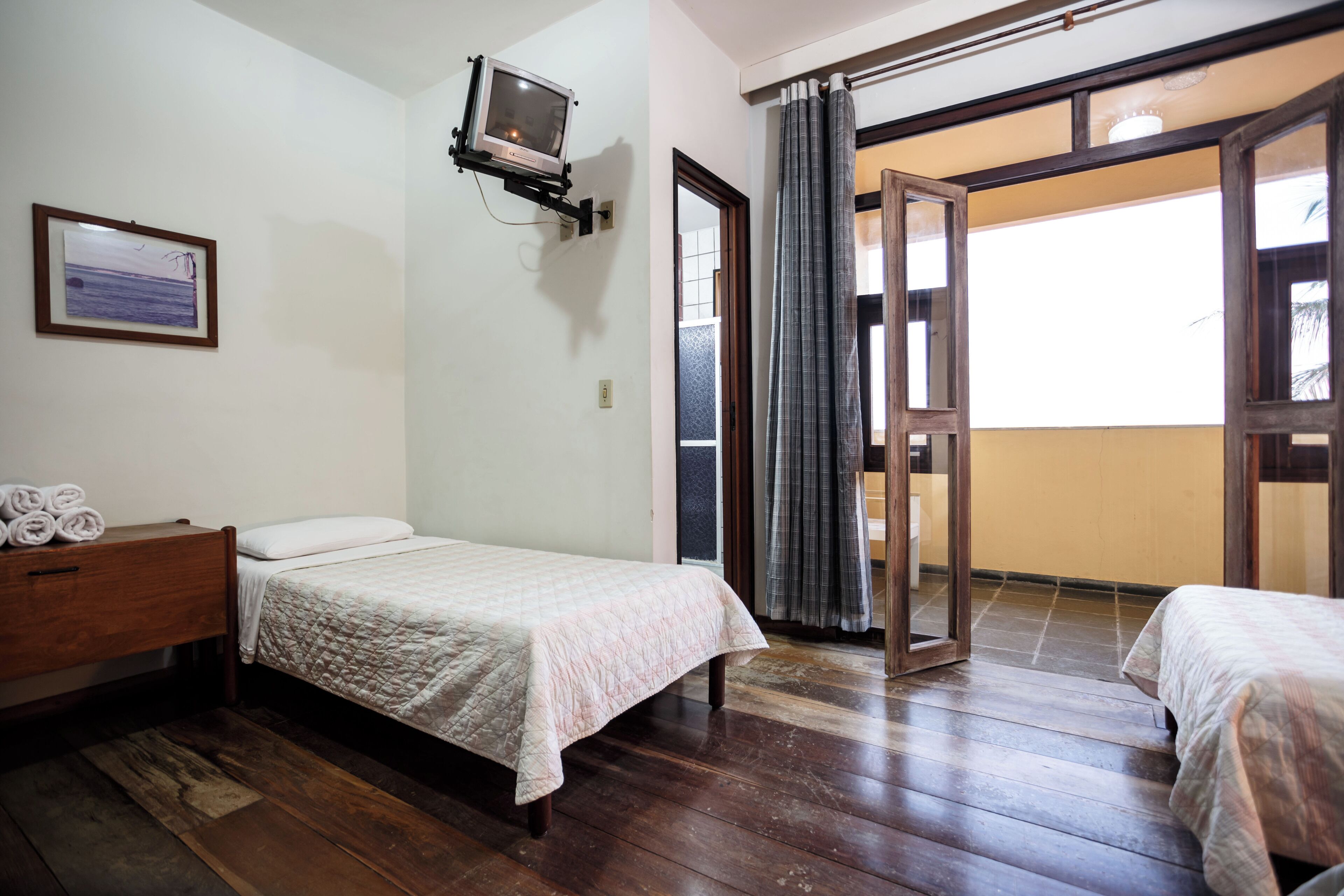 Una habitación con una cama, un aparador de madera, un televisor montado en la pared y un ventanal corredizo que da a un espacio al aire libre.
