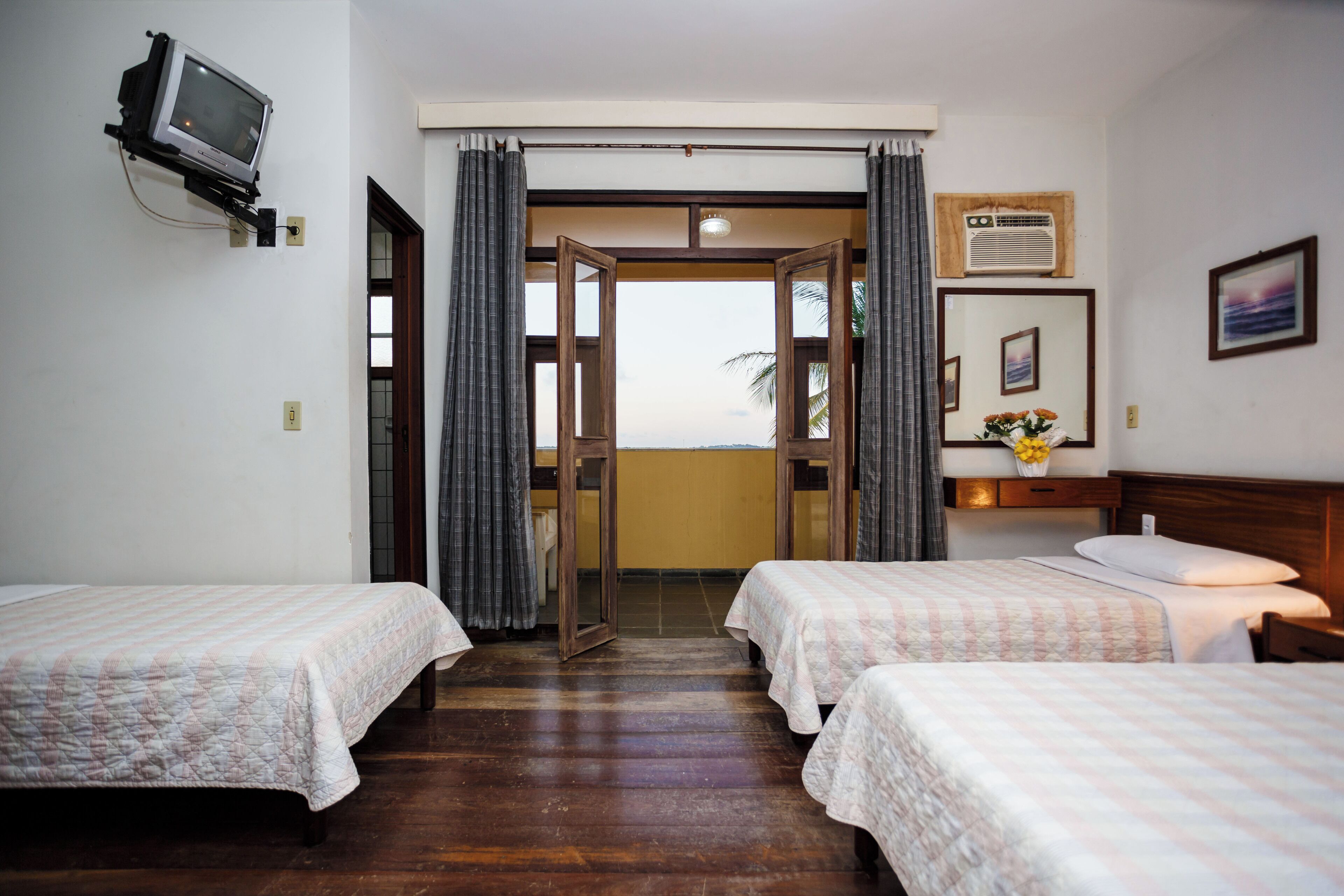 Habitación de hotel con dos camas, televisión, ventana con cortinas, piso de madera y vistas al exterior.