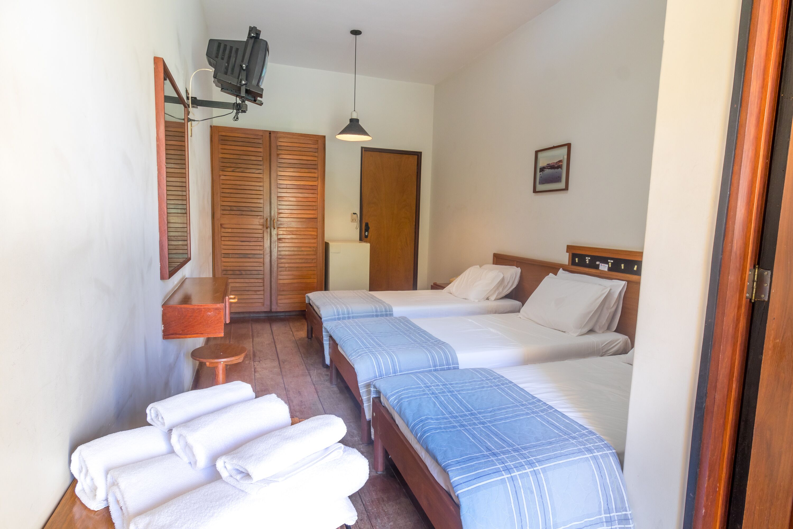 A hotel room with two beds, a wooden wardrobe, a small table, and a mirror.