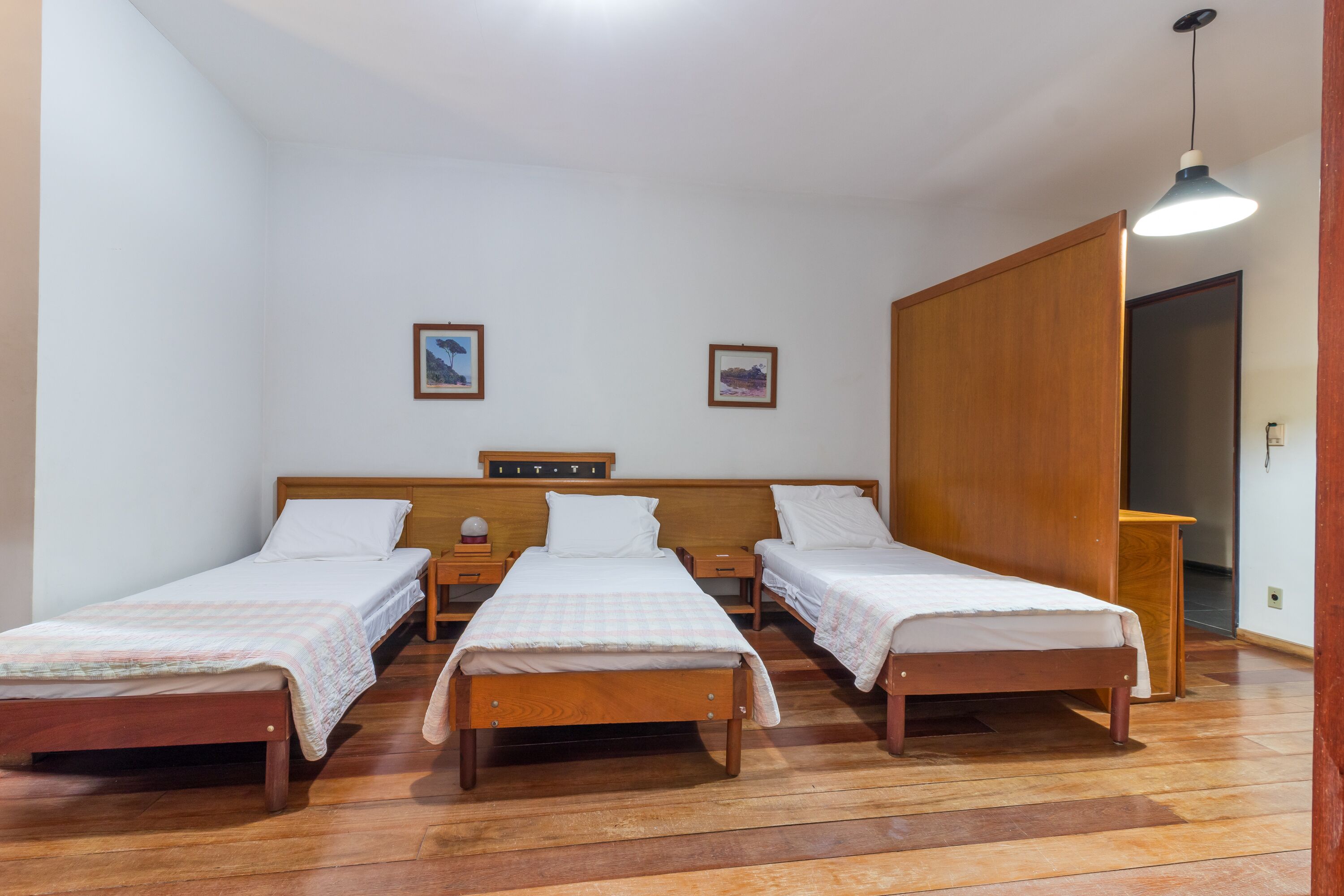 Una habitación con tres camas de madera, paredes blancas y un armario de madera.