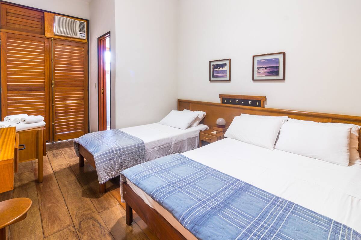 Habitación de hotel con dos camas individuales, muebles de madera, un escritorio con silla y un armario con puerta corredera.
