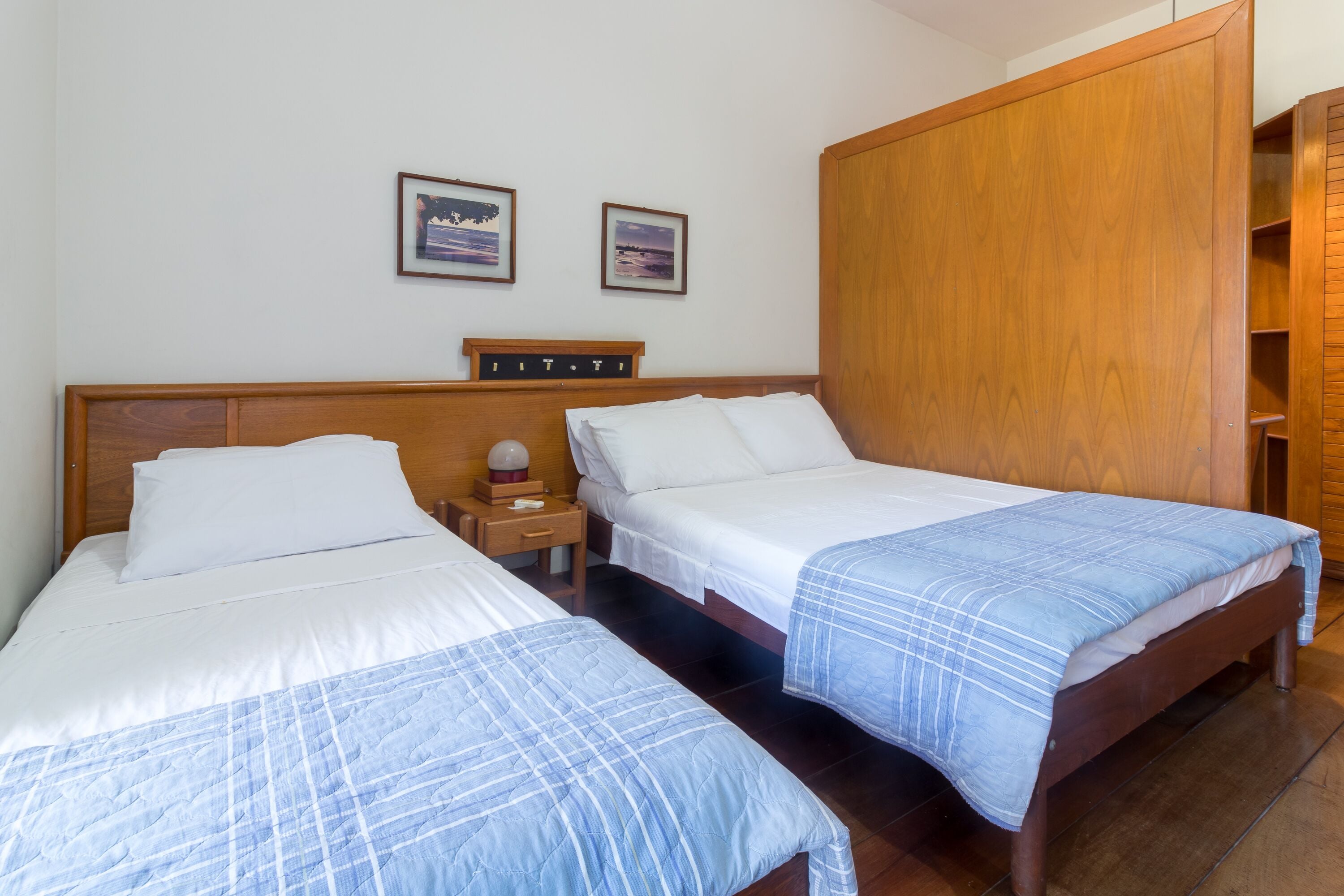 Habitación de hotel con dos camas, cabeceros de madera, ropa de cama blanca y un armario de madera.