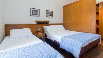 Habitación de hotel con dos camas, cabeceros de madera, ropa de cama blanca y un armario de madera.