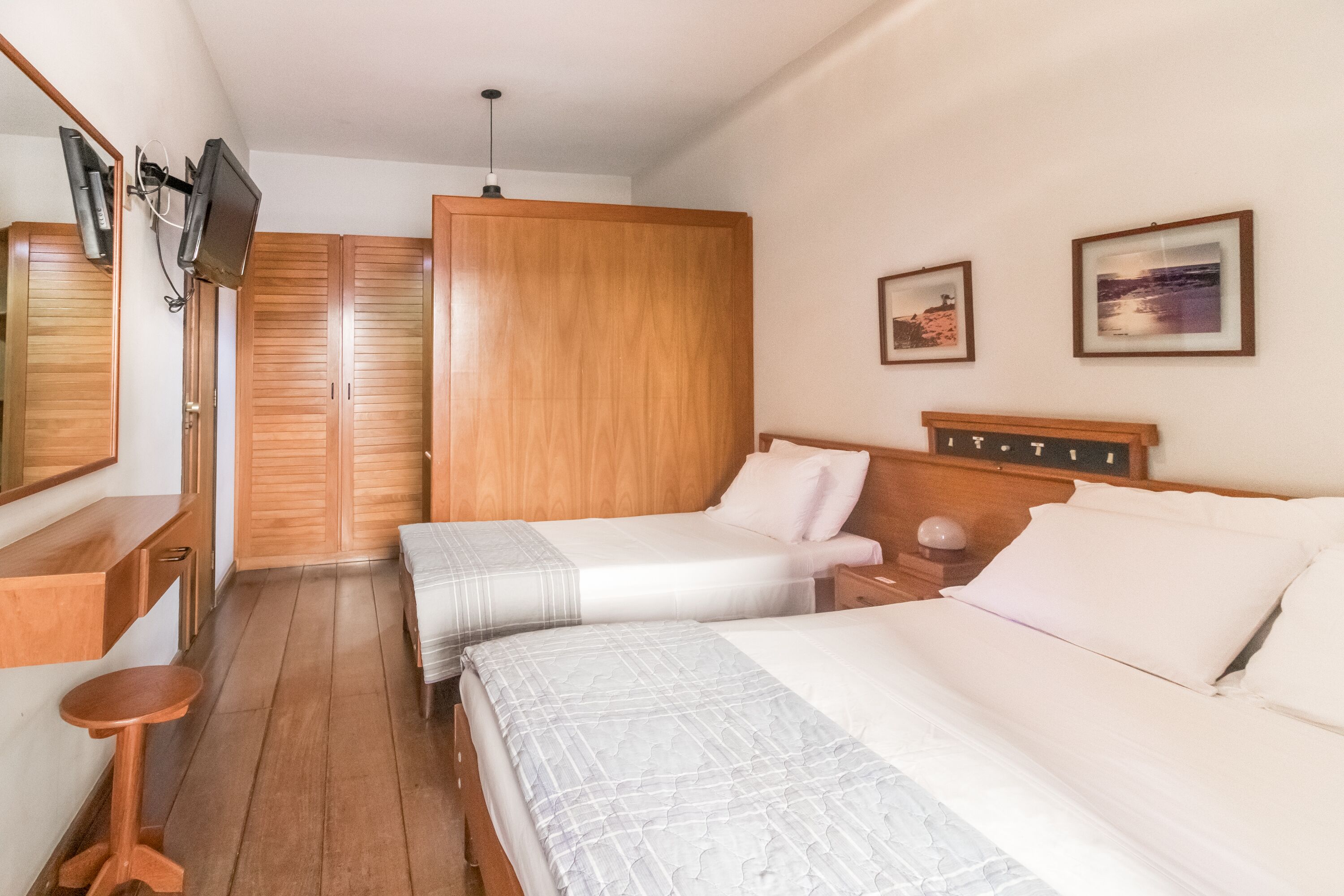 Un dormitorio con dos camas, un armario de madera, un televisor montado en la pared y cuadros enmarcados.