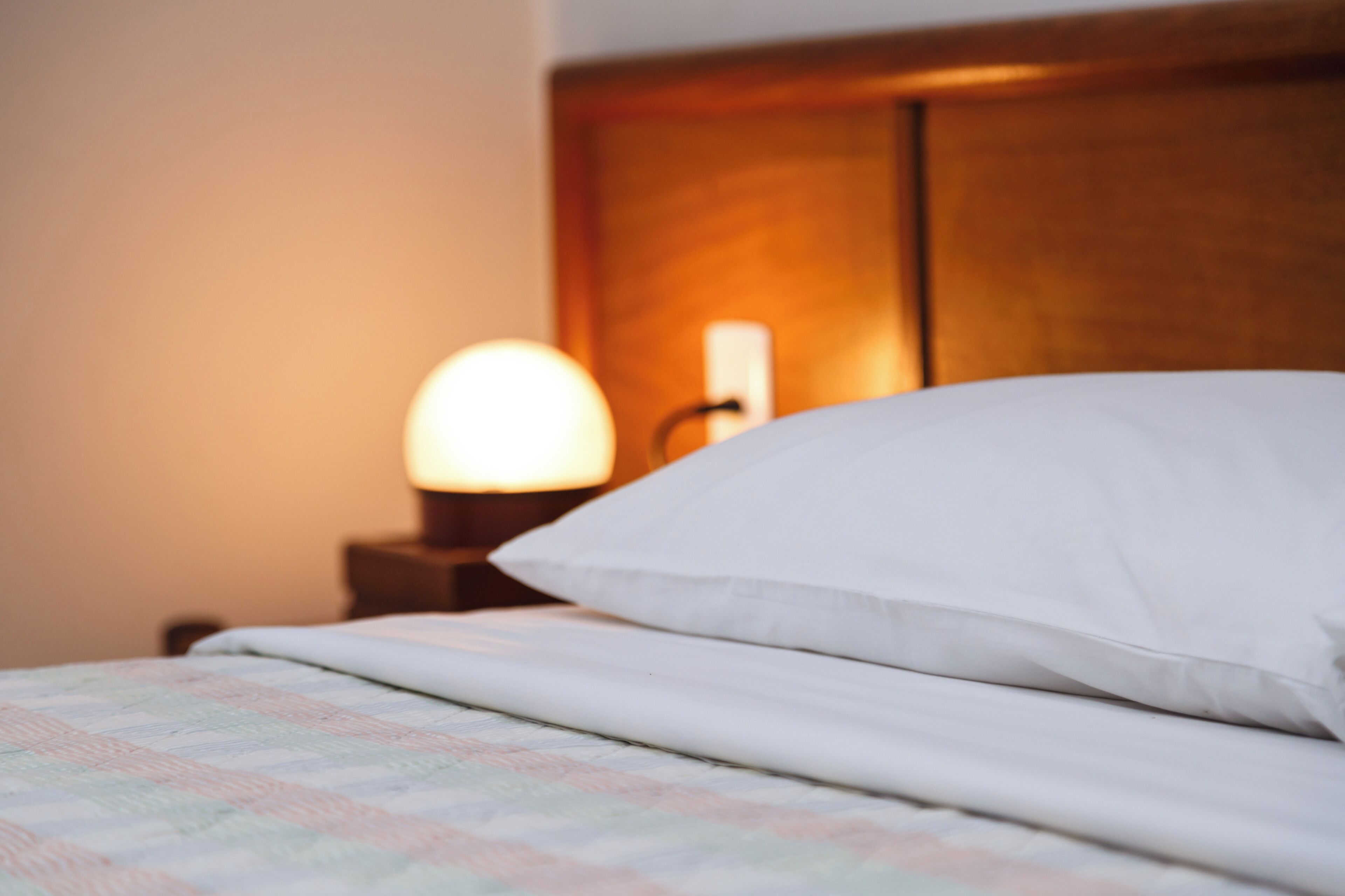 Una cama bien hecha con un almohadón blanco y una colcha a cuadros.
