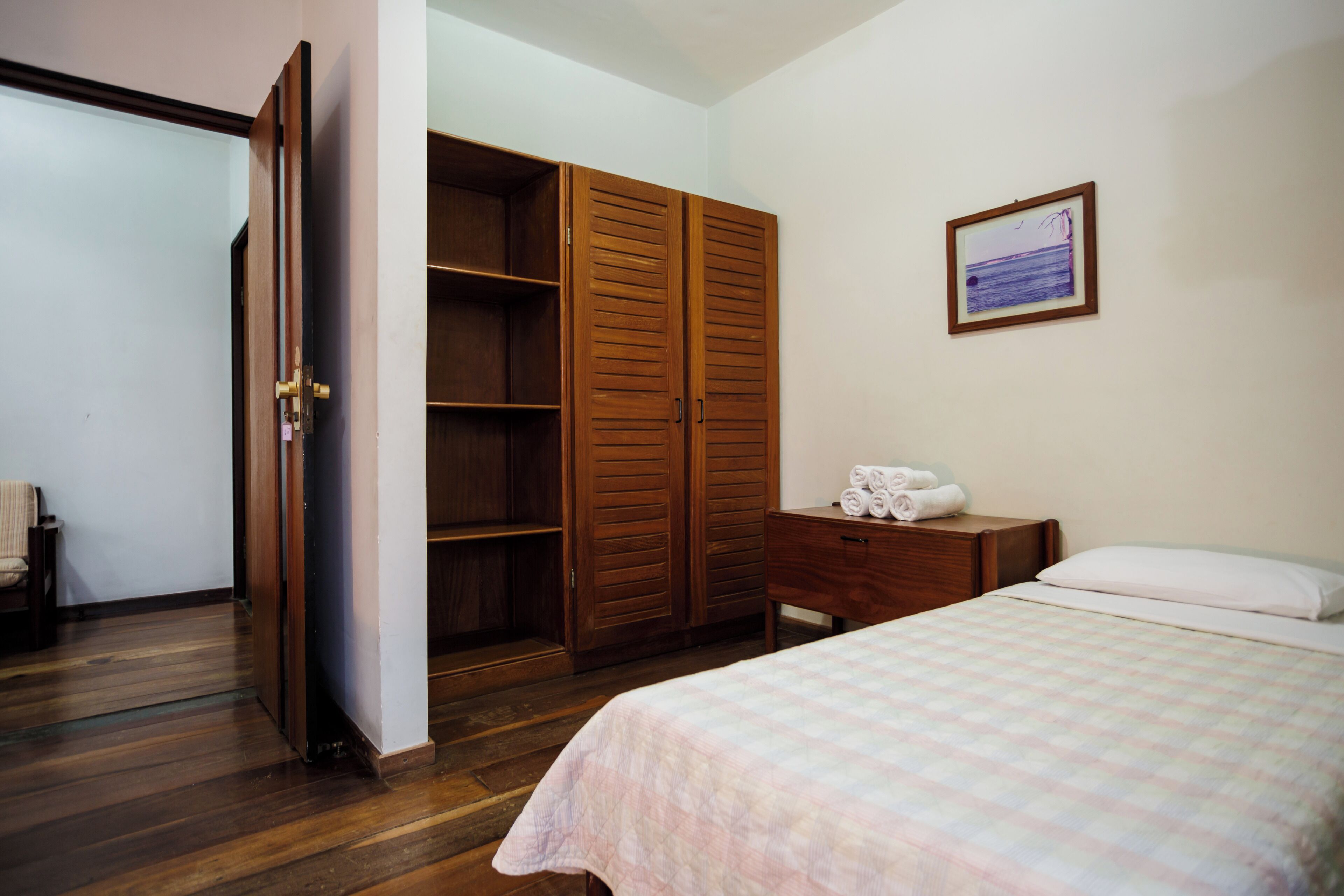 Un dormitorio con cama, armario de madera, mesita de noche y un cuadro en la pared.