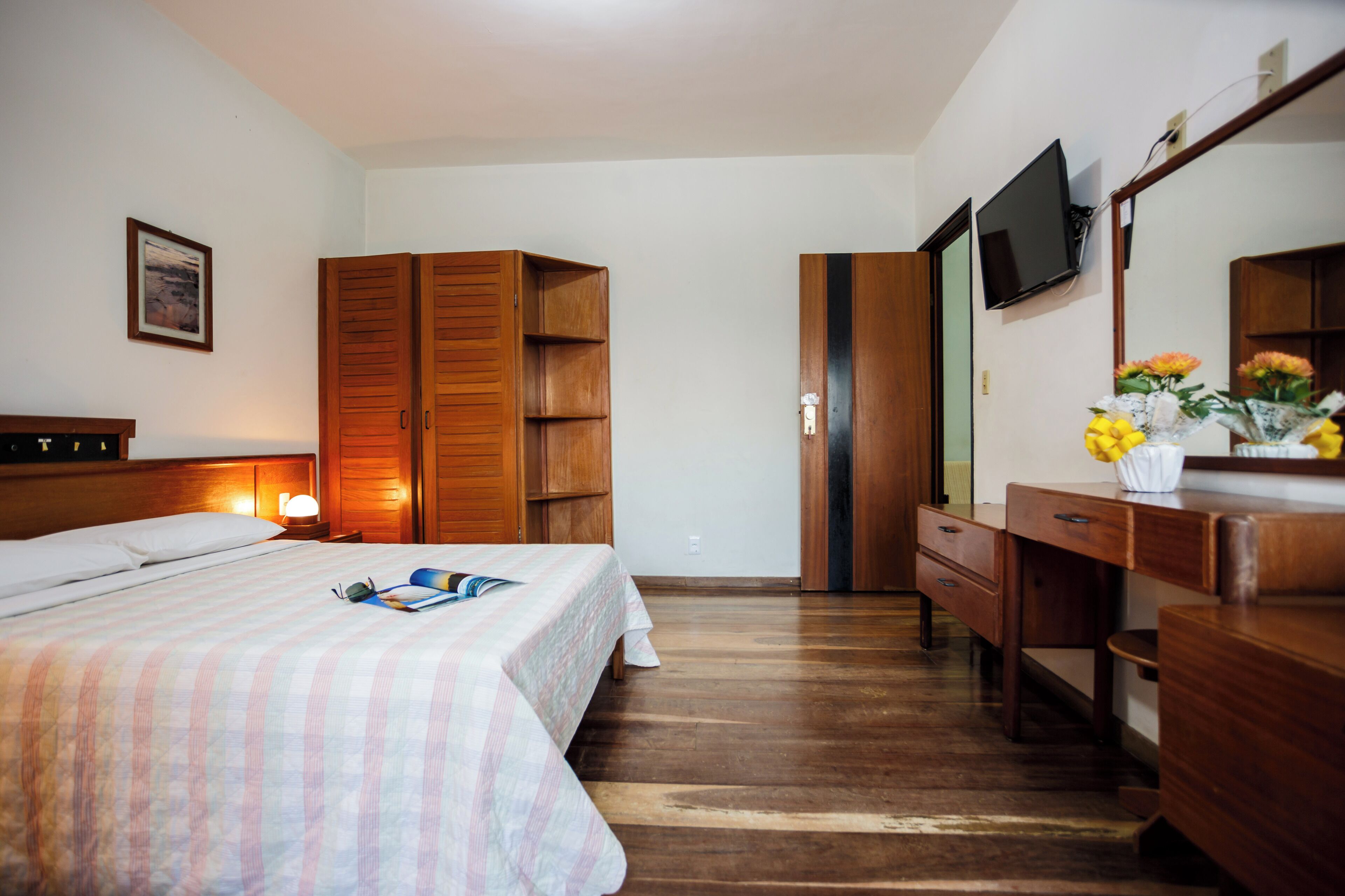 Una habitación de hotel con cama, armario de madera, escritorio y televisión en la pared.