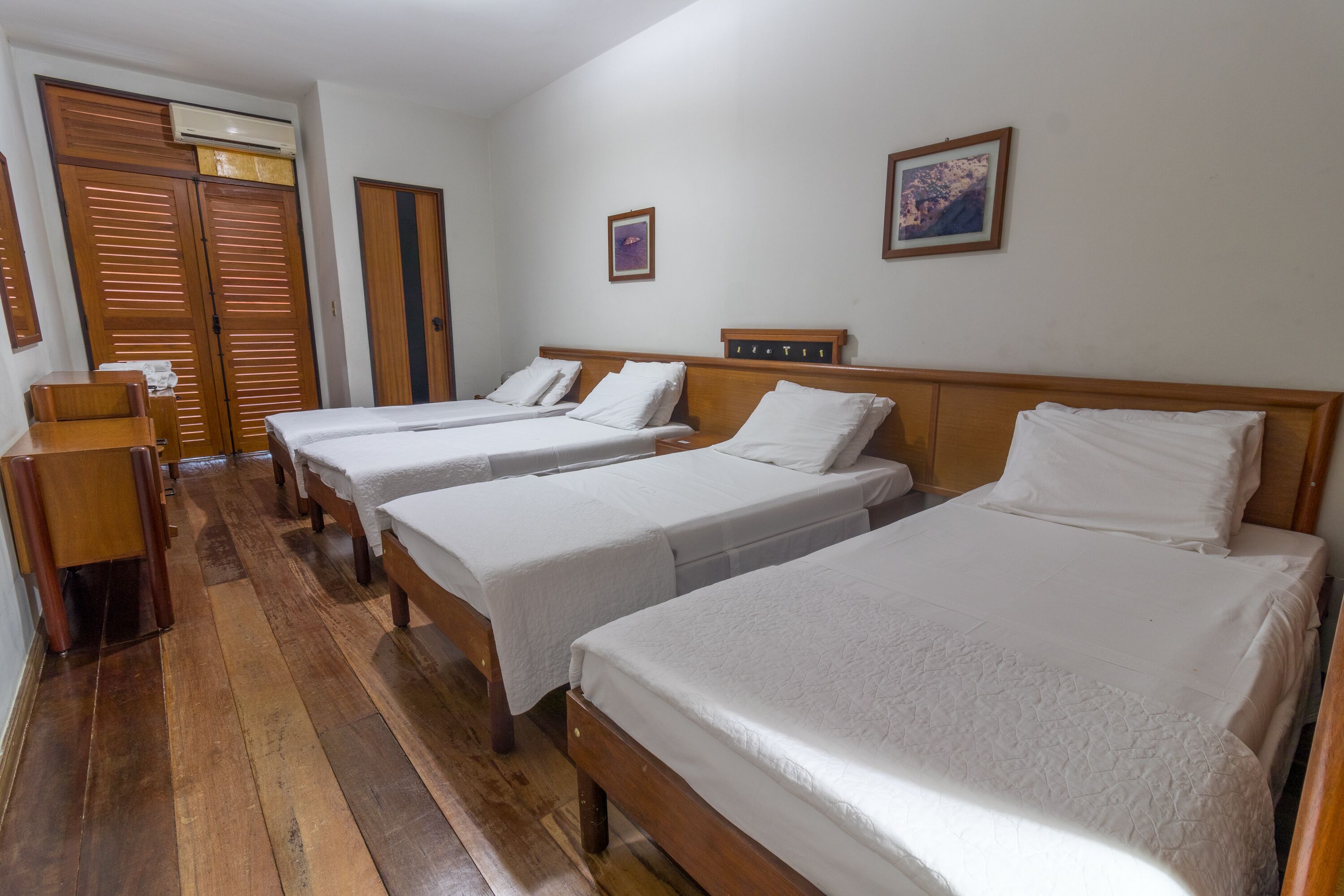 Habitación de hotel con tres camas individuales, suelo de madera, un armario de madera y un escritorio pequeño.