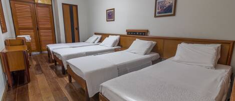 Habitación de hotel con tres camas individuales, suelo de madera, un armario de madera y un escritorio pequeño.