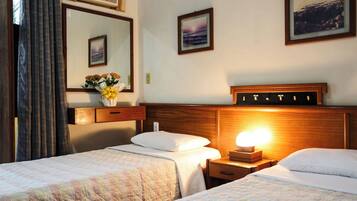 A hotel room with two beds, a nightstand with a lamp, a mirror, and framed pictures on the wall.