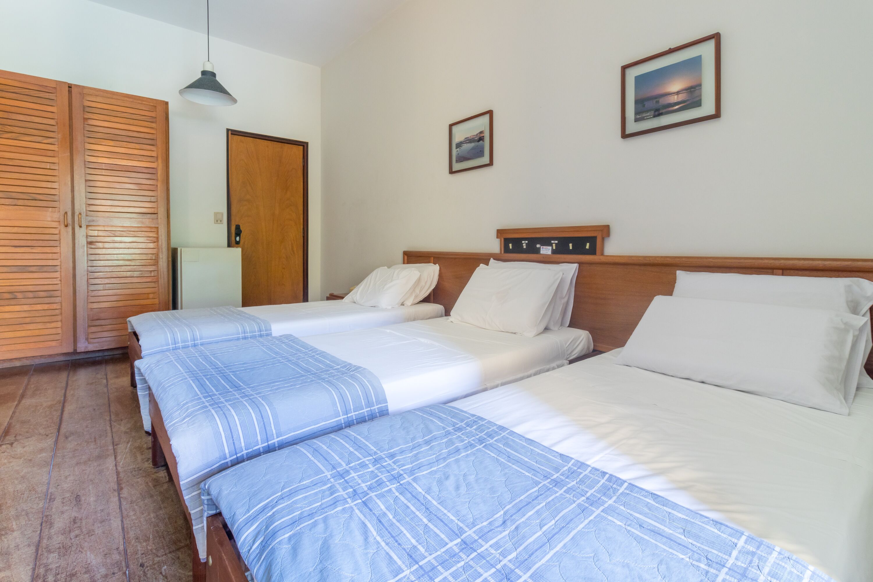 A hotel room with two beds, wooden wardrobe, and a picture on the wall.