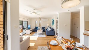 A modern living room with a TV, sofas, and a dining area with a table set for a meal. - Columbia Views,  2/9 Columbia Close - Aircon, WIFI, Netflix, Views & Boat Parking (Nelson Bay)