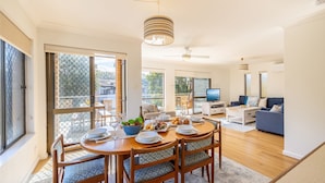A spacious living area with a dining table set for a meal, a television, and a comfortable seating area with a sofa and chairs. - Columbia Views,  2/9 Columbia Close - Aircon, WIFI, Netflix, Views & Boat Parking (Nelson Bay)
