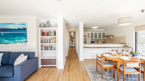 A modern living room with a sofa, a bookshelf, and a dining area with a table and chairs. - Columbia Views,  2/9 Columbia Close - Aircon, WIFI, Netflix, Views & Boat Parking (Nelson Bay)