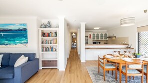 A modern living room with a sofa, a bookshelf, and a dining area with a table and chairs. - Columbia Views,  2/9 Columbia Close - Aircon, WIFI, Netflix, Views & Boat Parking (Nelson Bay)