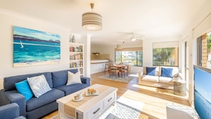 A modern living room with a sofa, coffee table, and a painting of a beach scene. - Columbia Views,  2/9 Columbia Close - Aircon, WIFI, Netflix, Views & Boat Parking (Nelson Bay)
