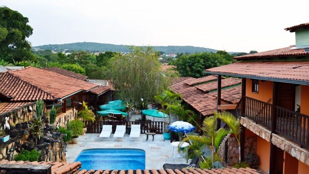 A pool area with a view of a mountainous landscape, surrounded by buildings with terracotta roofs and stone walls. - Pousada Vila Velha (Pirenópolis)