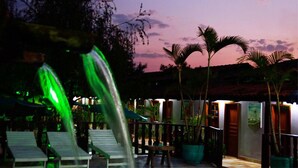 A poolside area with lounge chairs, a water feature, and potted plants against a sunset sky. - Pousada Vila Velha (Pirenópolis)