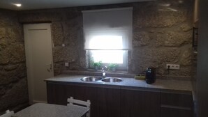 Una cocina con pared de piedra, una ventana, un lavabo y una silla.